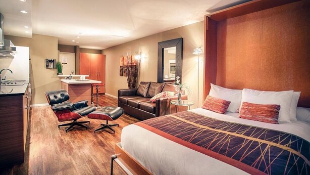 A hotel room with a large bed, a sofa, a desk with a chair, and a small table with a lamp. - Nuvo Hotel & Suites (Calgary)