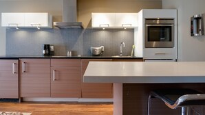 A modern kitchen with wooden cabinets, a stainless steel oven, and a built-in coffee maker. - Nuvo Hotel & Suites (Calgary)