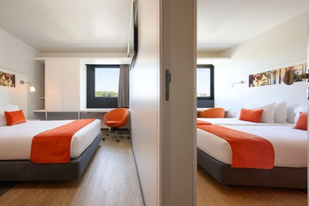 A hotel room with two beds, a desk, and a chair.