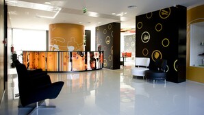 A modern lobby with a reception desk, a black lounge chair, and a seating area with a white sofa and a black armchair. - Star Inn Porto (Porto)