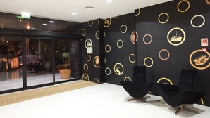 A modern reception area with a white reception desk, black chairs, and a black wall with gold circular patterns. - Star Inn Porto (Porto)
