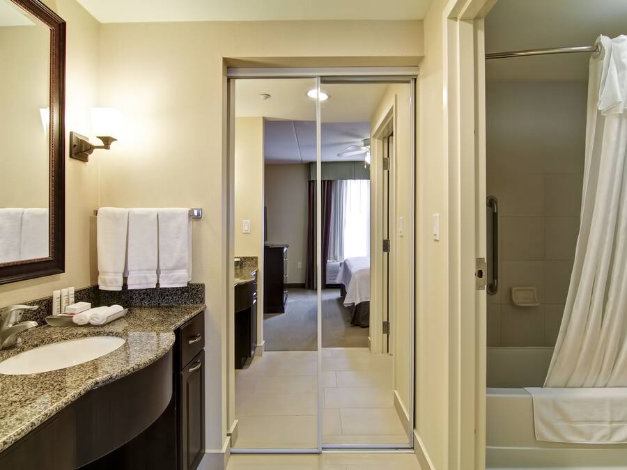 A modern bathroom with a granite countertop sink, a large mirror, and a glass shower enclosure.