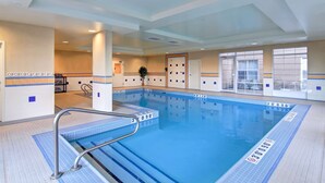 An indoor swimming pool with clear lane markings, a lifeguard stand, and a view of the outside through large windows.