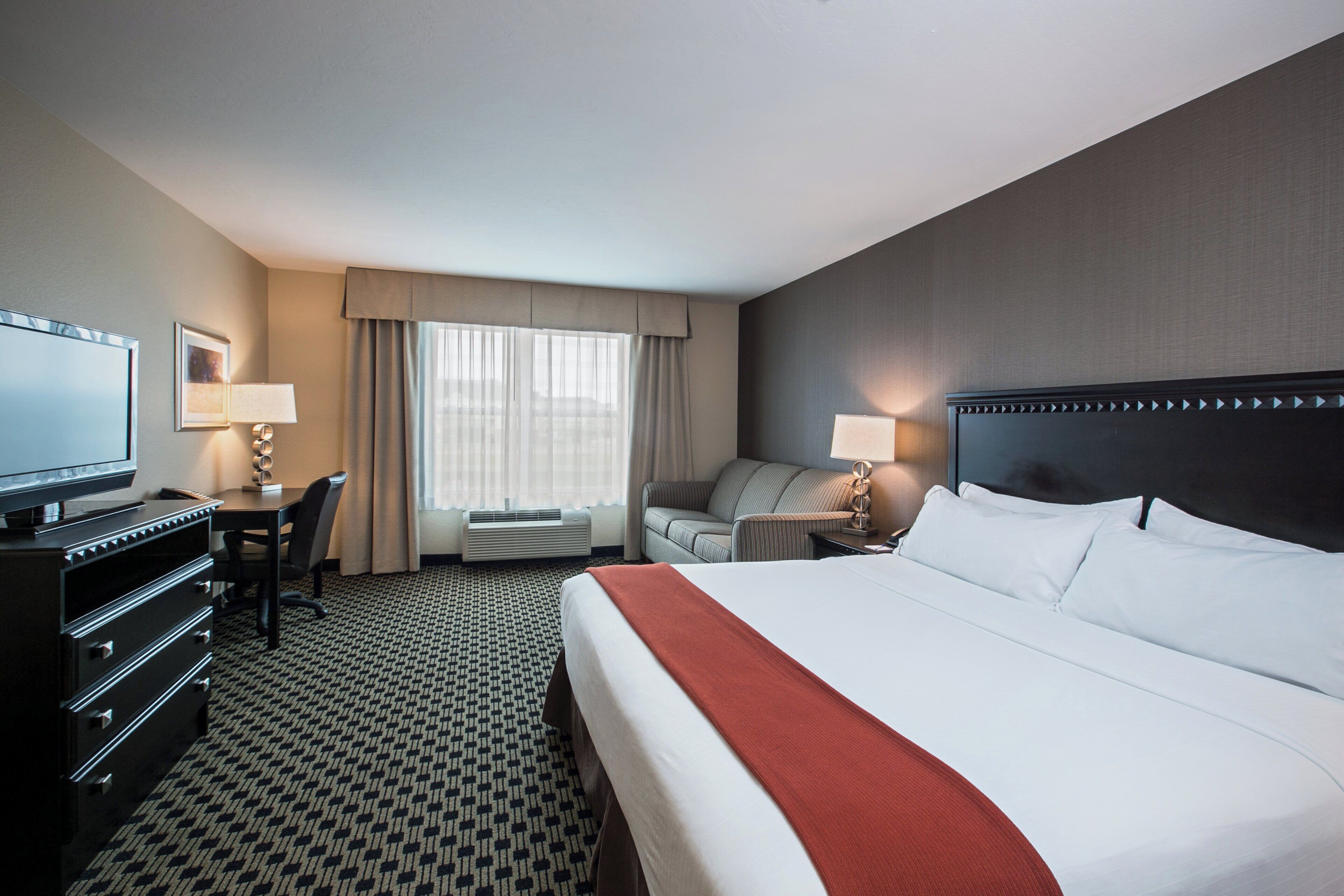 A hotel room with a large bed, a desk, a chair, a television, and a window with curtains.