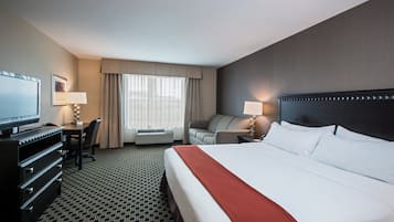 A hotel room with a large bed, a desk, a chair, a television, and a window with curtains.