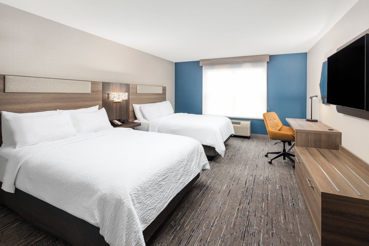A hotel room with two beds, a desk, a chair, a TV, and a window with curtains.