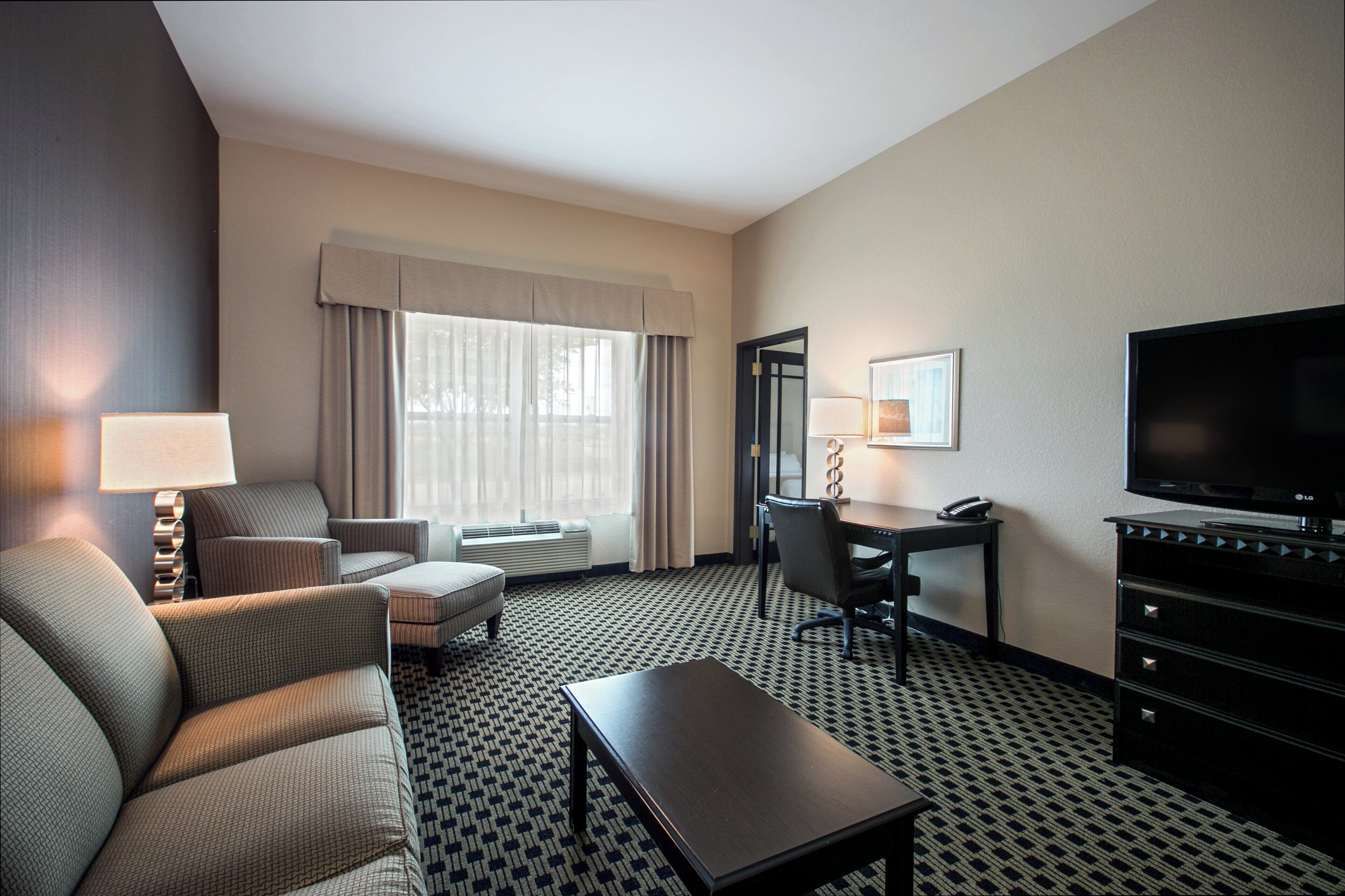 A hotel room with a sofa, a desk, a television, and a window with curtains.