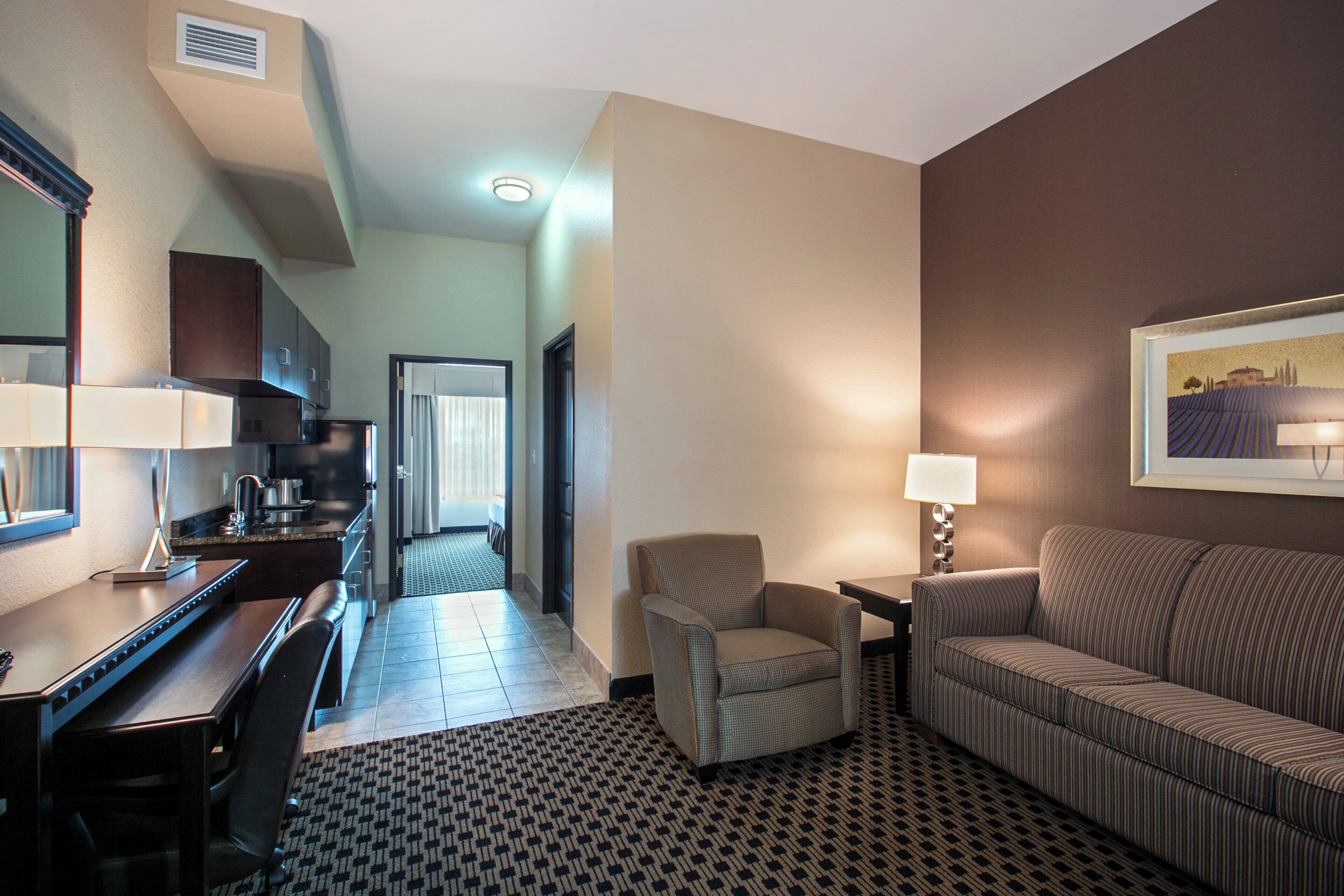 Een hotelkamer met een kitchenette, een eethoek, een bank, een stoel en een bed.