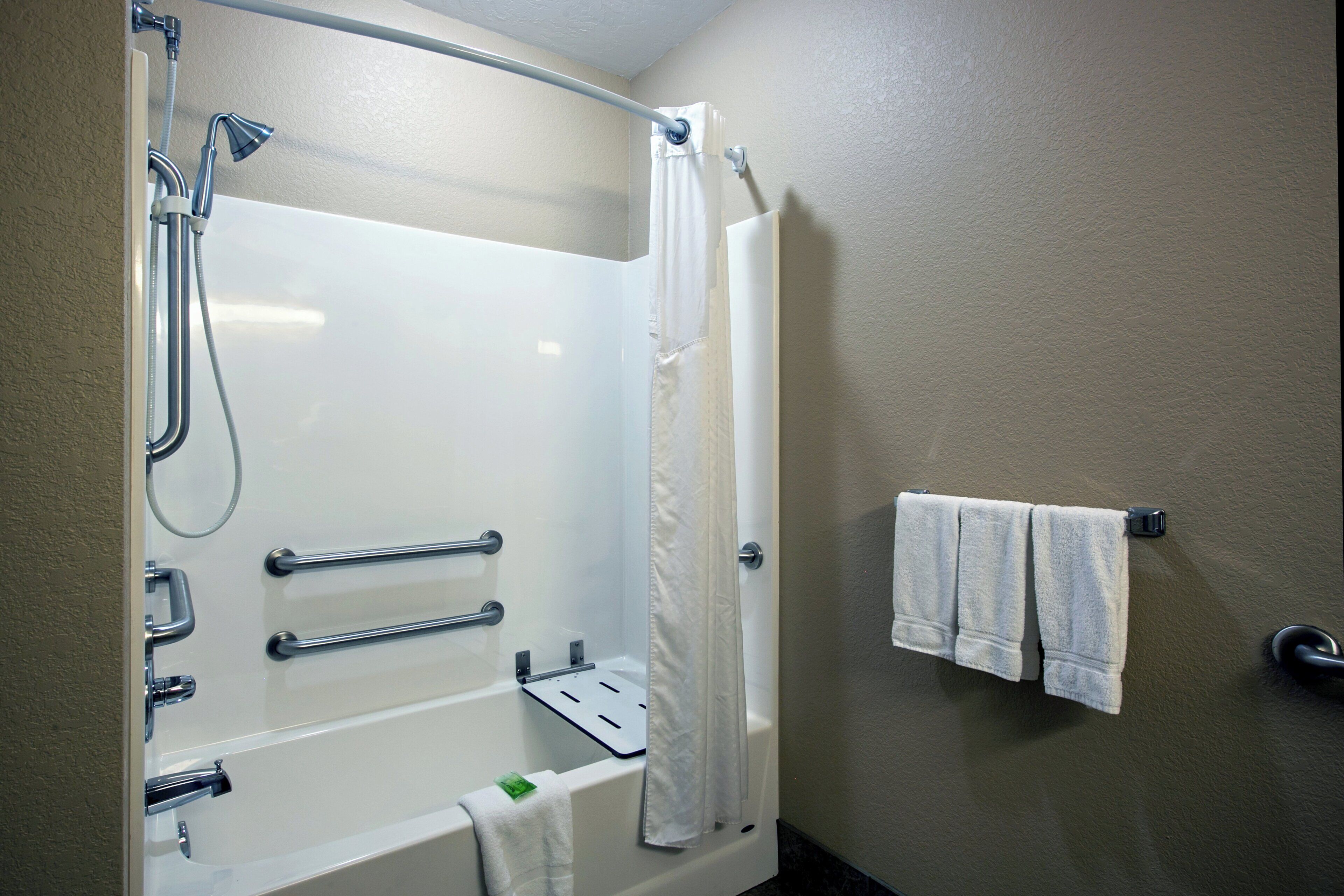 A bathroom with a bathtub, shower, grab bars, a towel rack, and a toilet.