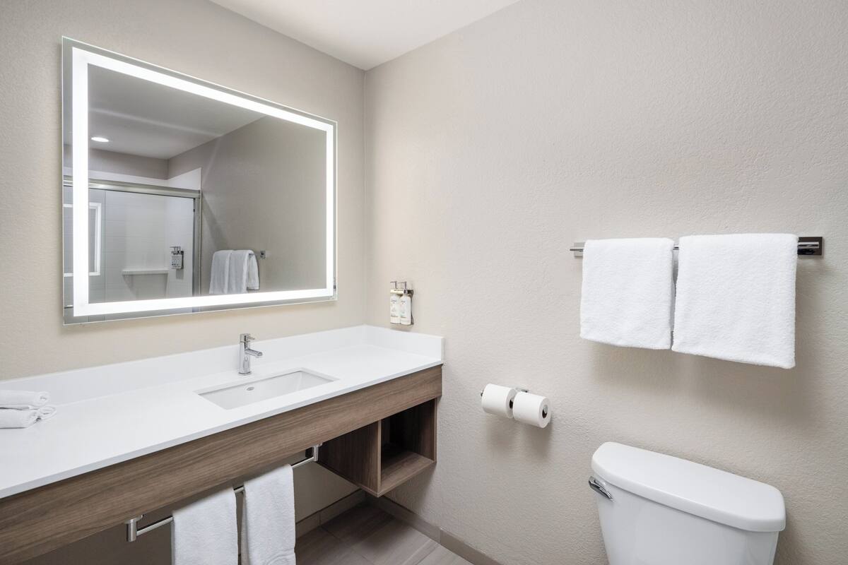A modern bathroom with a white sink, mirror, and toilet. There are two towels hanging on the wall.