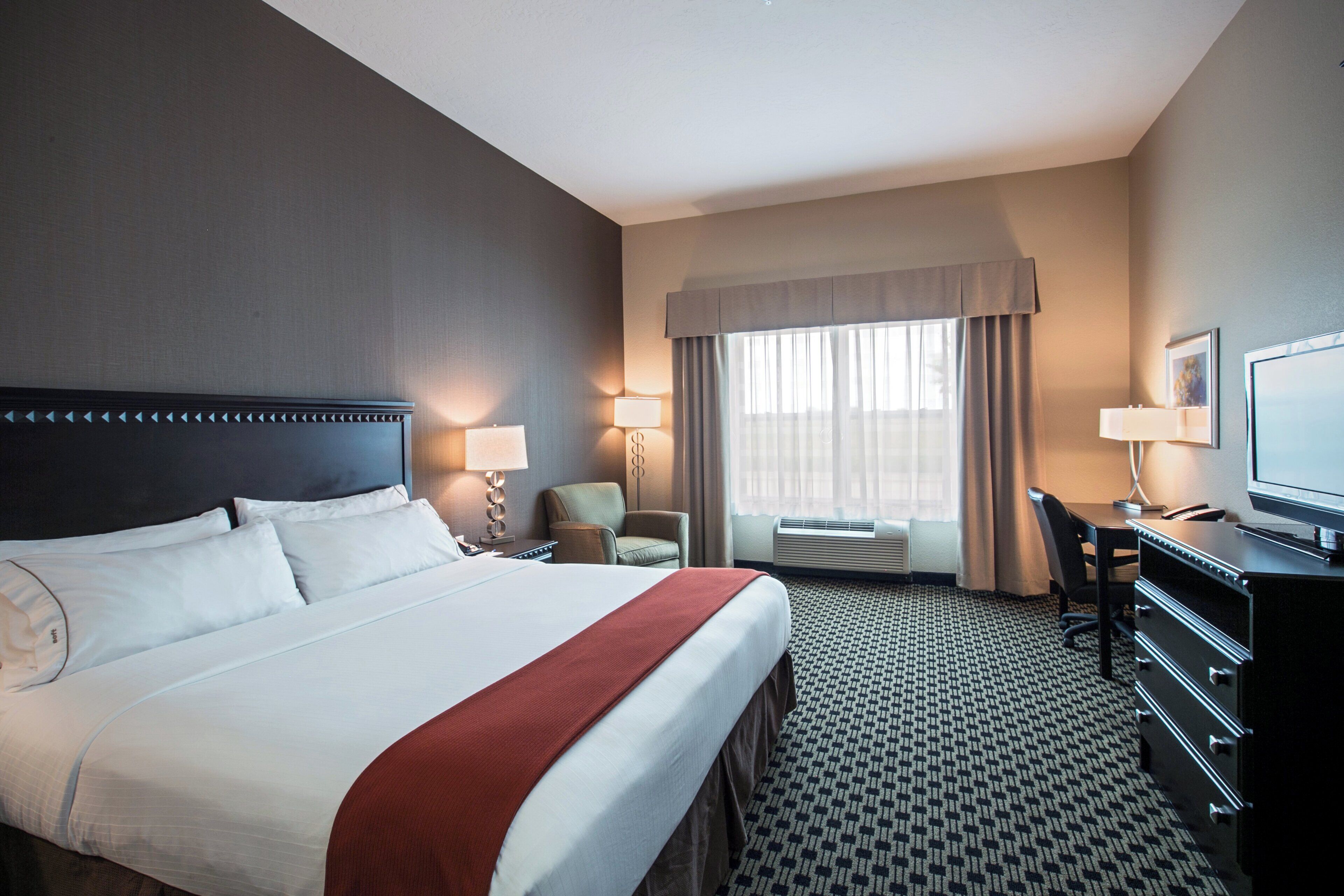 A hotel room with a large bed, a desk, a chair, a television, and a window with curtains.