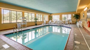 An indoor swimming pool with clear blue water, surrounded by lounge chairs and a sunlit room with large windows.