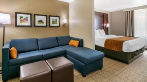 A hotel room with a sectional sofa, a bed, and three framed pictures on the wall.
