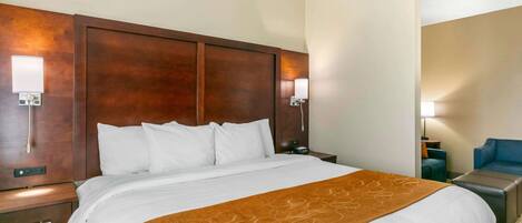 A hotel room with a large bed, a wooden headboard, two bedside tables, a nightstand, a desk, and a chair.