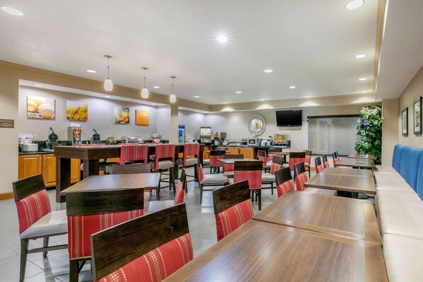 A restaurant with multiple dining tables and chairs, a kitchen area, and a television screen.