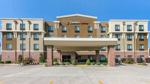 A multi-story hotel with a central entrance, marked by a canopy and a sign reading "Comfort Suites".