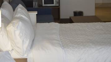 A hotel room with a bed, pillows, a microwave, and a small kitchenette area.
