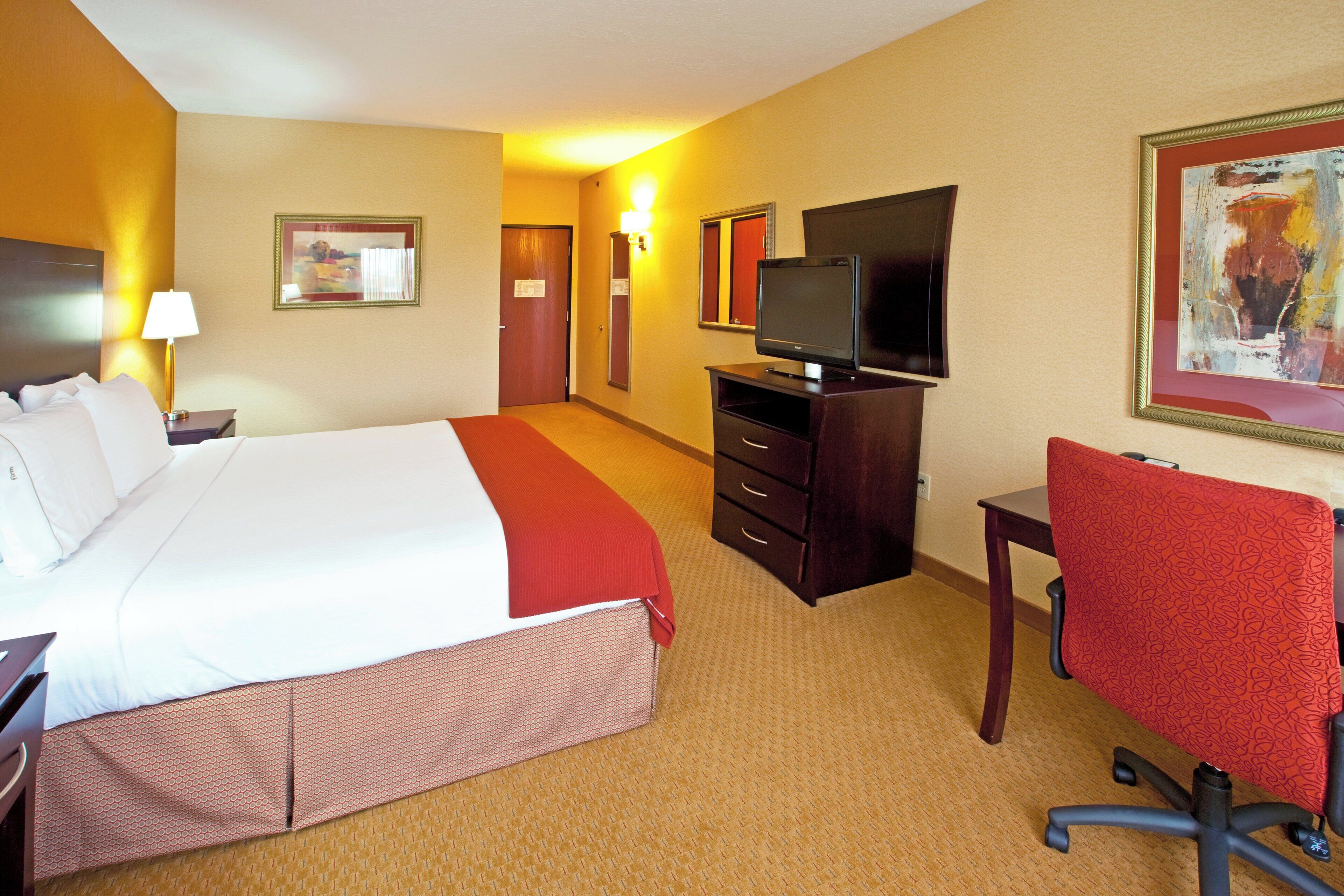 A hotel room with a bed, a desk, a chair, a television, and a painting on the wall.