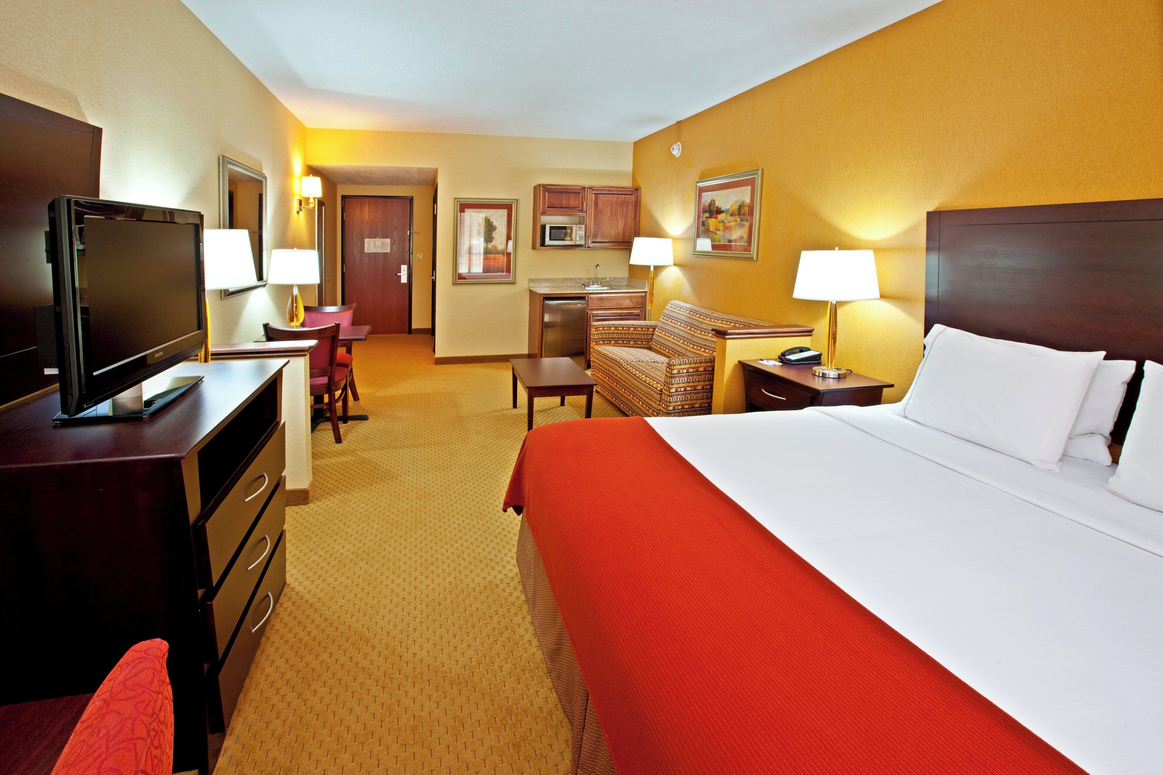 A hotel room with a bed, a desk, a television, a chair, a sofa, and a microwave.