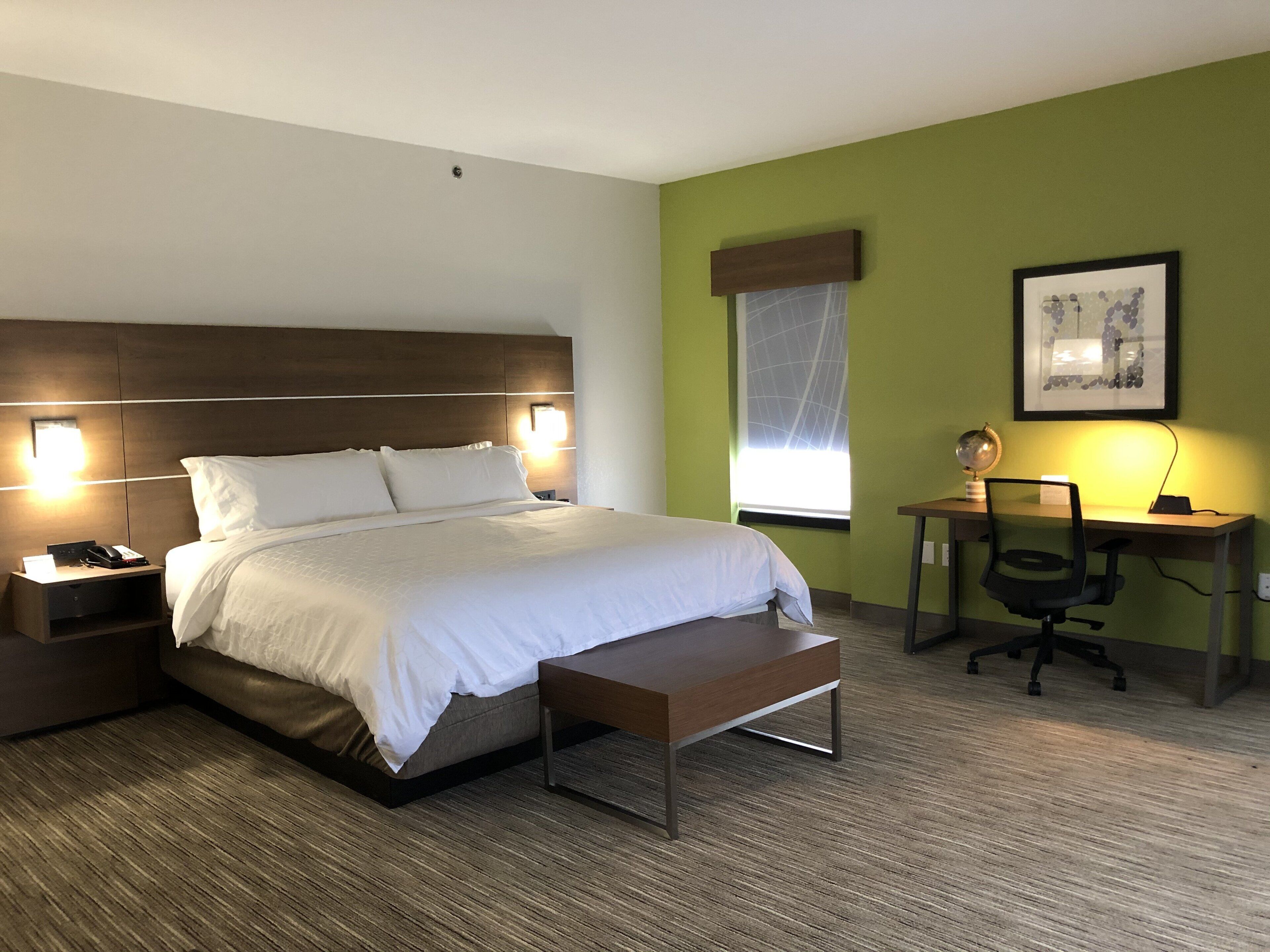 Quarto de hotel com cama, mesas de cabeceira, escrivaninha com cadeira, janela com vista e um quadro na parede.