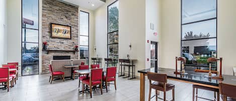 Un comedor moderno con sillas rojas, una barra negra y una pared de piedra con chimenea.