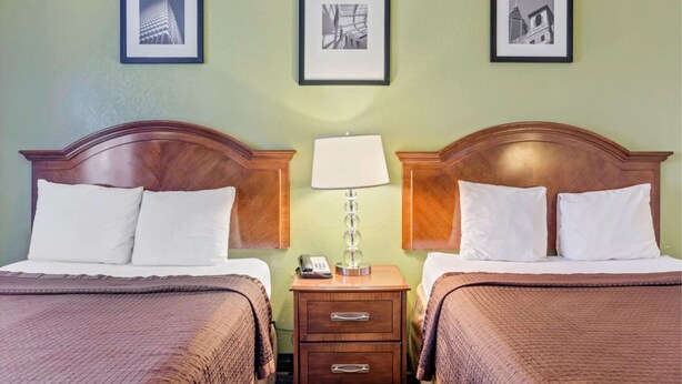 A hotel room with two beds, a nightstand with a lamp, and framed pictures on the wall.