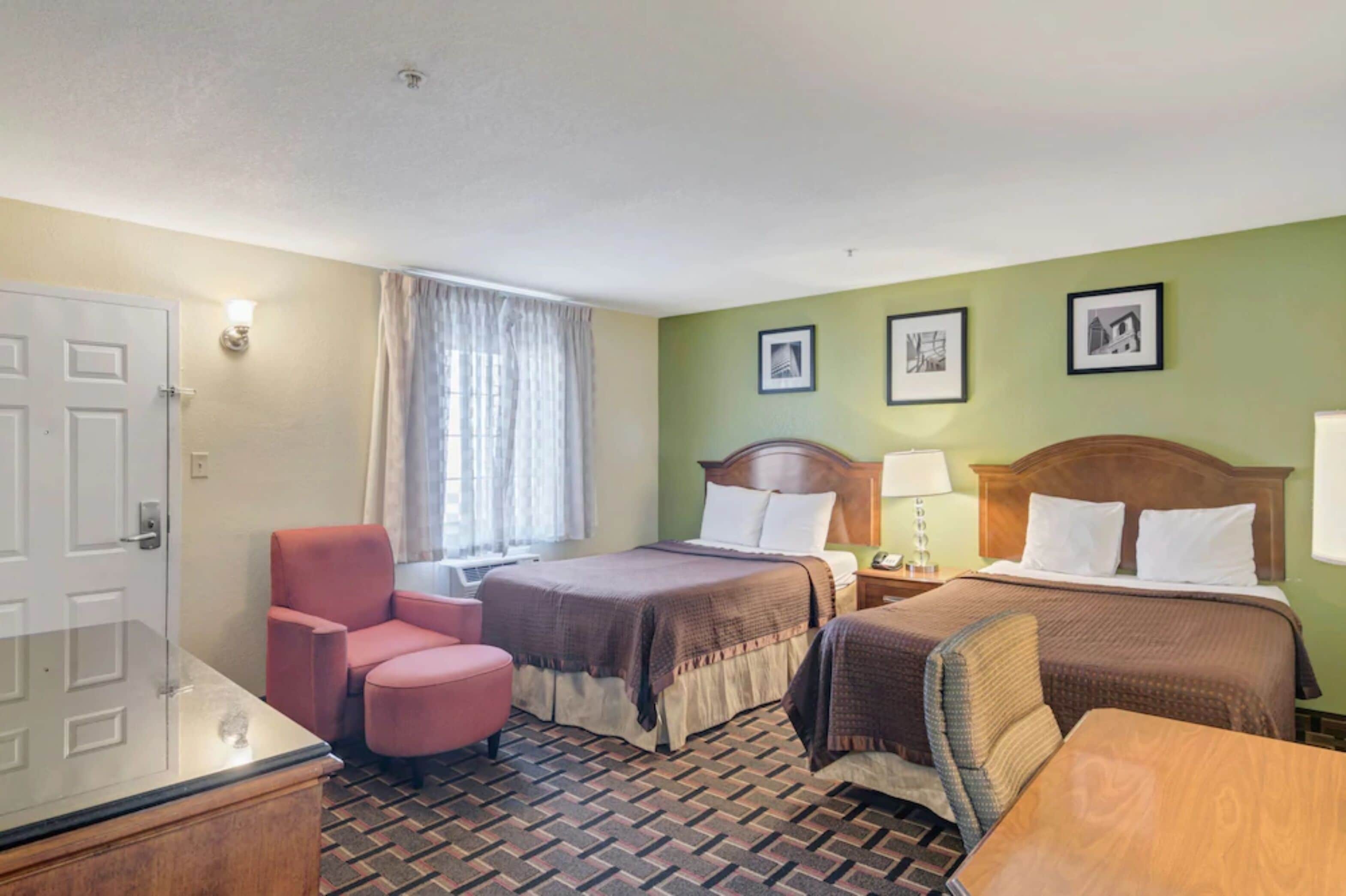 A hotel room with two beds, a desk, a chair, and a window with curtains.