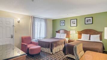 A hotel room with two beds, a desk, a chair, and a window with curtains.