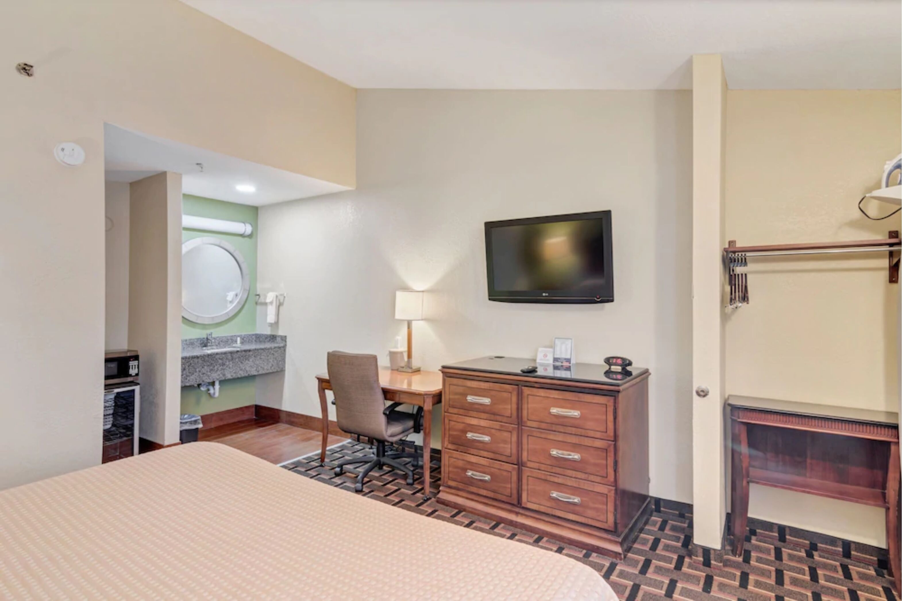 Habitación de hotel con cama, escritorio, silla, televisión, cómoda y baño visible a través de una puerta abierta.