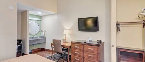 Habitación de hotel con cama, escritorio, silla, televisión, cómoda y baño visible a través de una puerta abierta.