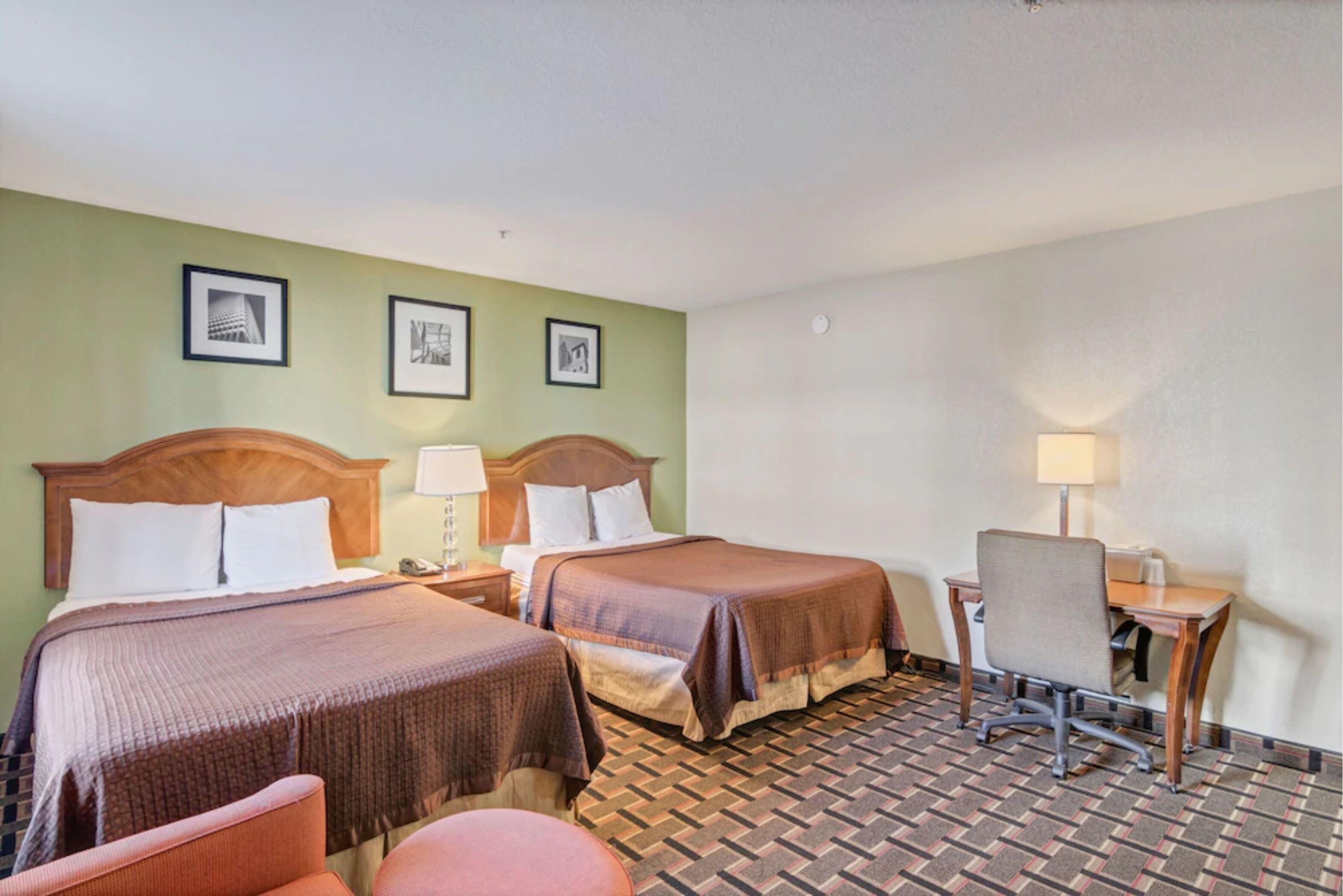 Quarto de hotel com duas camas, uma escrivaninha, uma cadeira e uma pequena mesa.