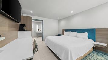 Habitación de hotel moderna con una cama grande, un escritorio, un televisor de pantalla plana y un baño visible a través de una puerta abierta.
