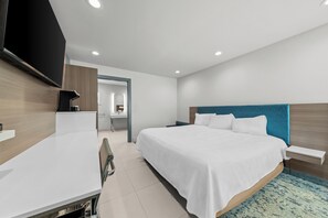 Une chambre d’hôtel moderne dotée d’un grand lit, d’un bureau, d’un téléviseur à écran plat et d’une salle de bain visible à travers une porte ouverte.