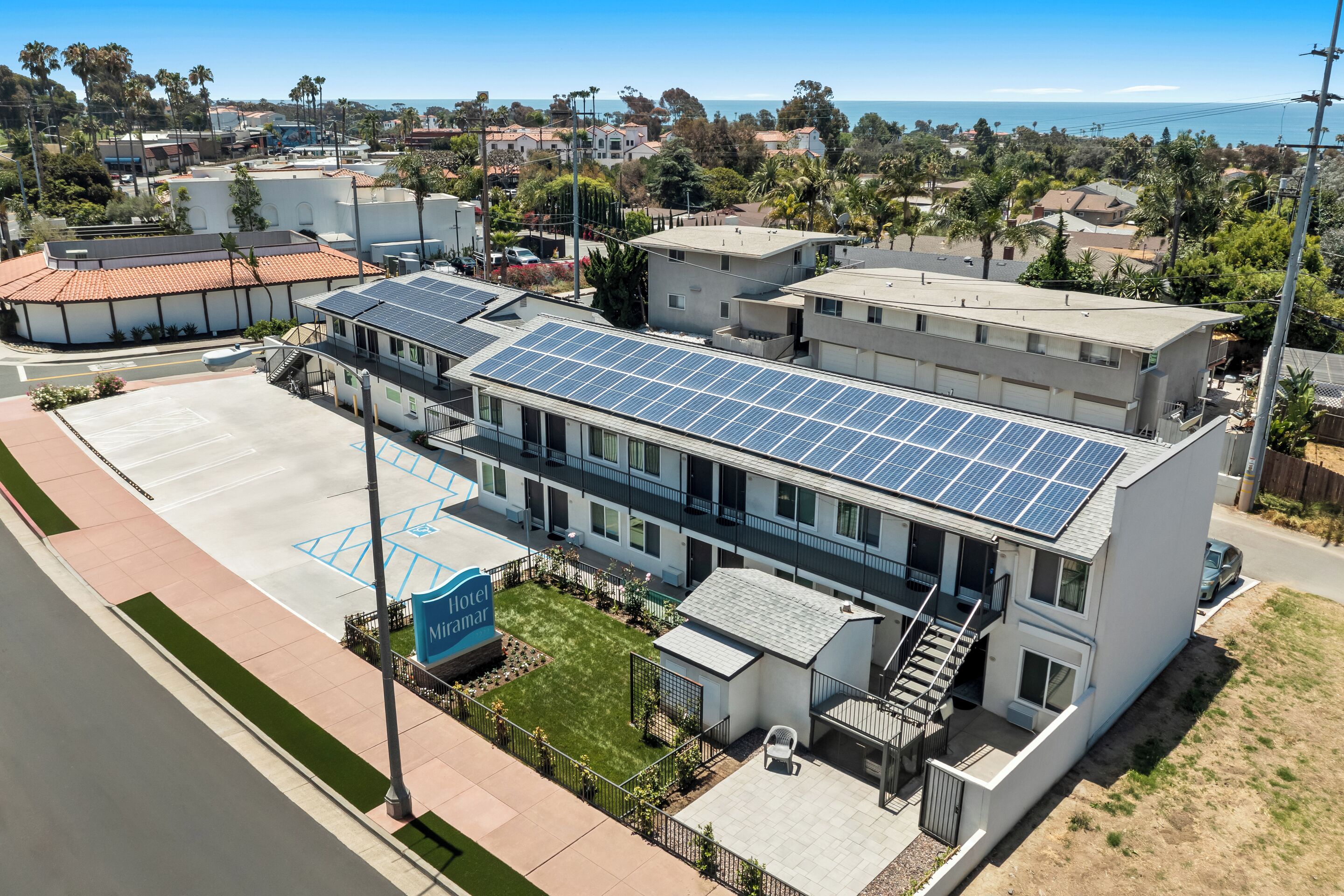 A hotel with a rooftop solar panel array, a parking lot, and a view of the ocean.