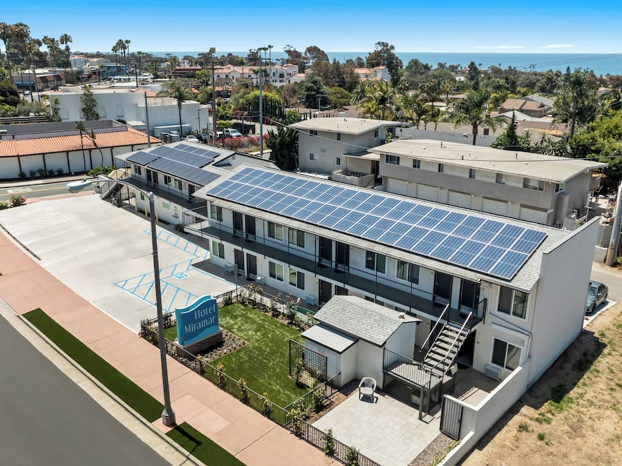A hotel with a rooftop solar panel array, a parking lot, and a view of the ocean.