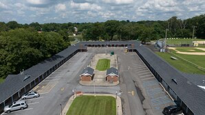 A large parking lot with multiple rows of parking spaces, a central grassy area, and a building with a sloped roof. - Budget Inn and Suites (Mount Ephraim)