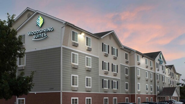 Un hotel de varios pisos con techo plano y un letrero que dice 'Woodspring Suites'.