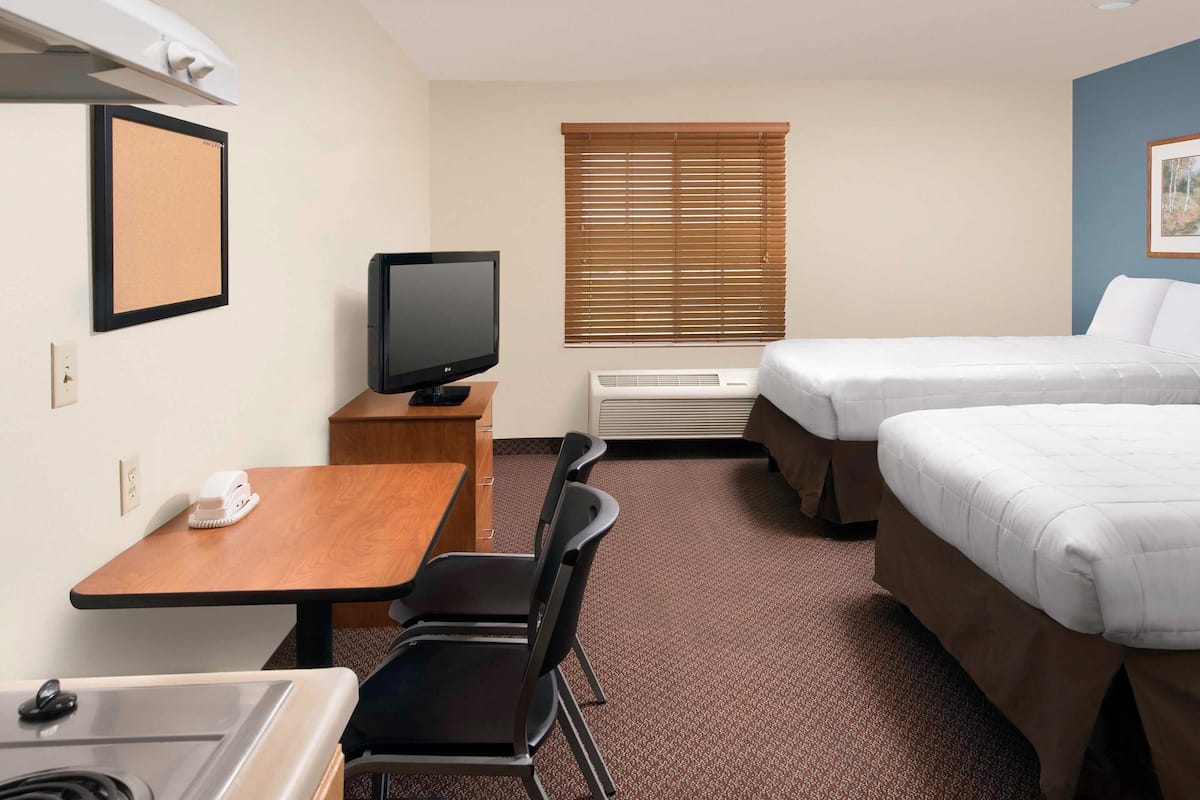 A hotel room with a bed, a desk with a computer, a chair, a television, and a window with blinds.