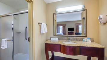 A hotel bathroom with a glass shower enclosure, a large mirror, and a vanity with a sink and towel rack.