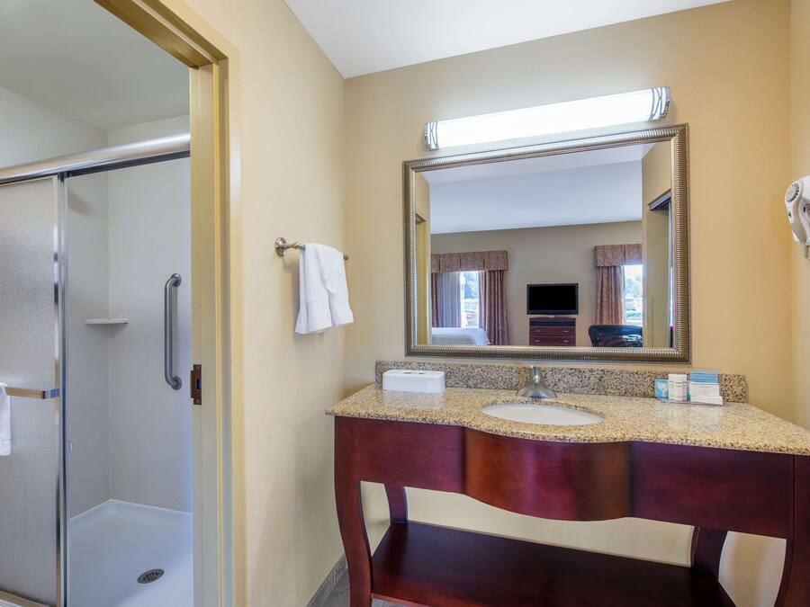 A hotel bathroom with a glass shower enclosure, a large mirror, and a vanity with a sink and towel rack.