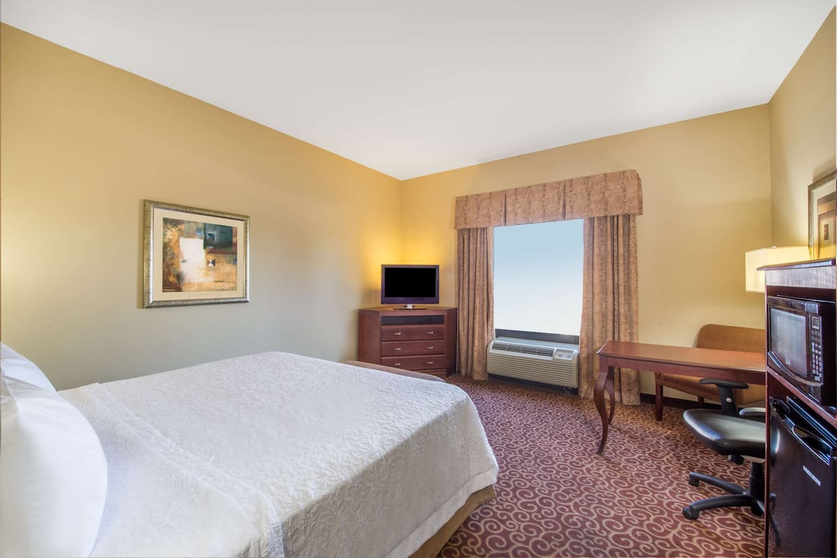 A hotel room with a bed, a desk with a chair, a television, and an air conditioning unit.