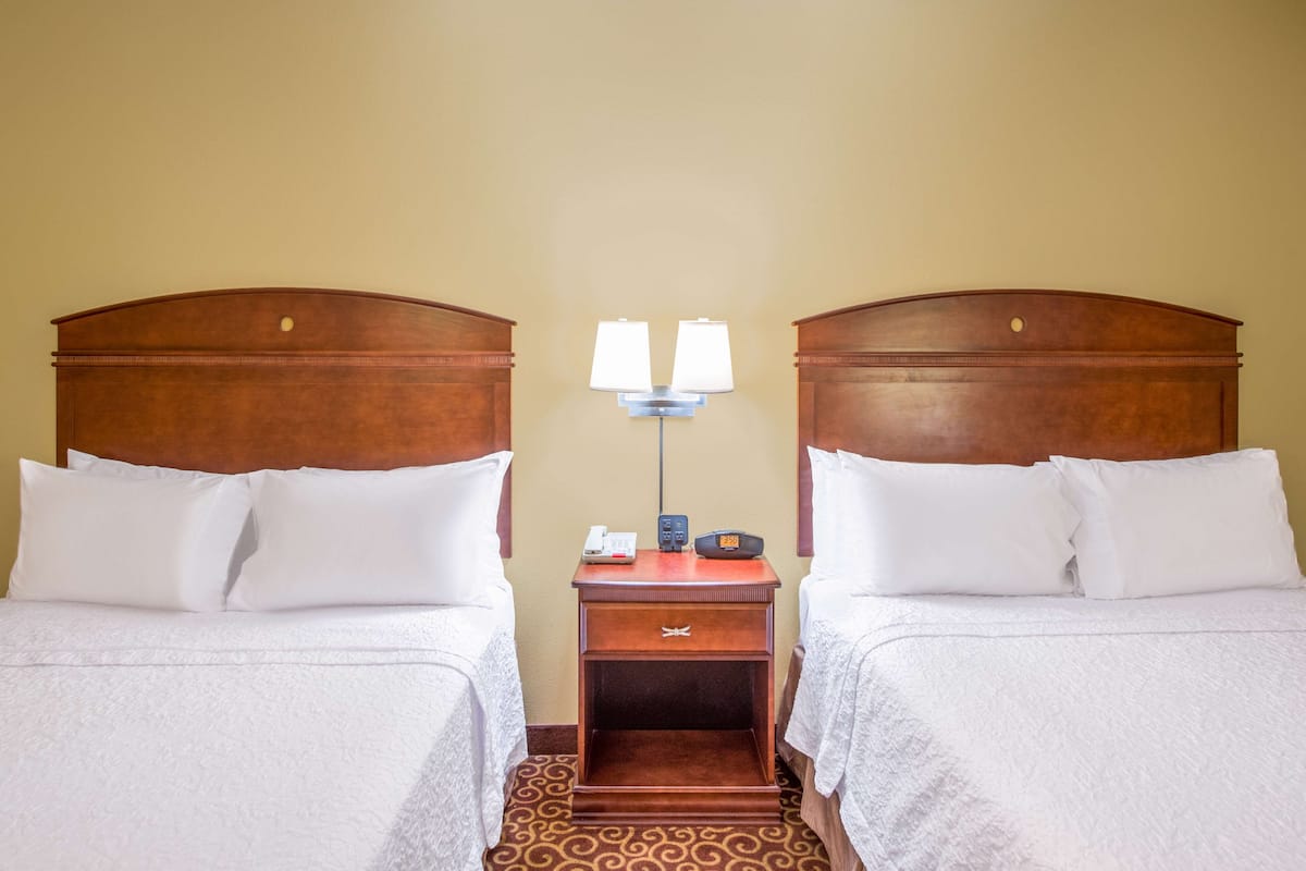 A hotel room with two beds, a nightstand with a lamp, a phone, and a radio.