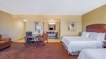 A hotel room with two beds, a desk with a chair, a small sofa, and a bathroom visible through an open door.