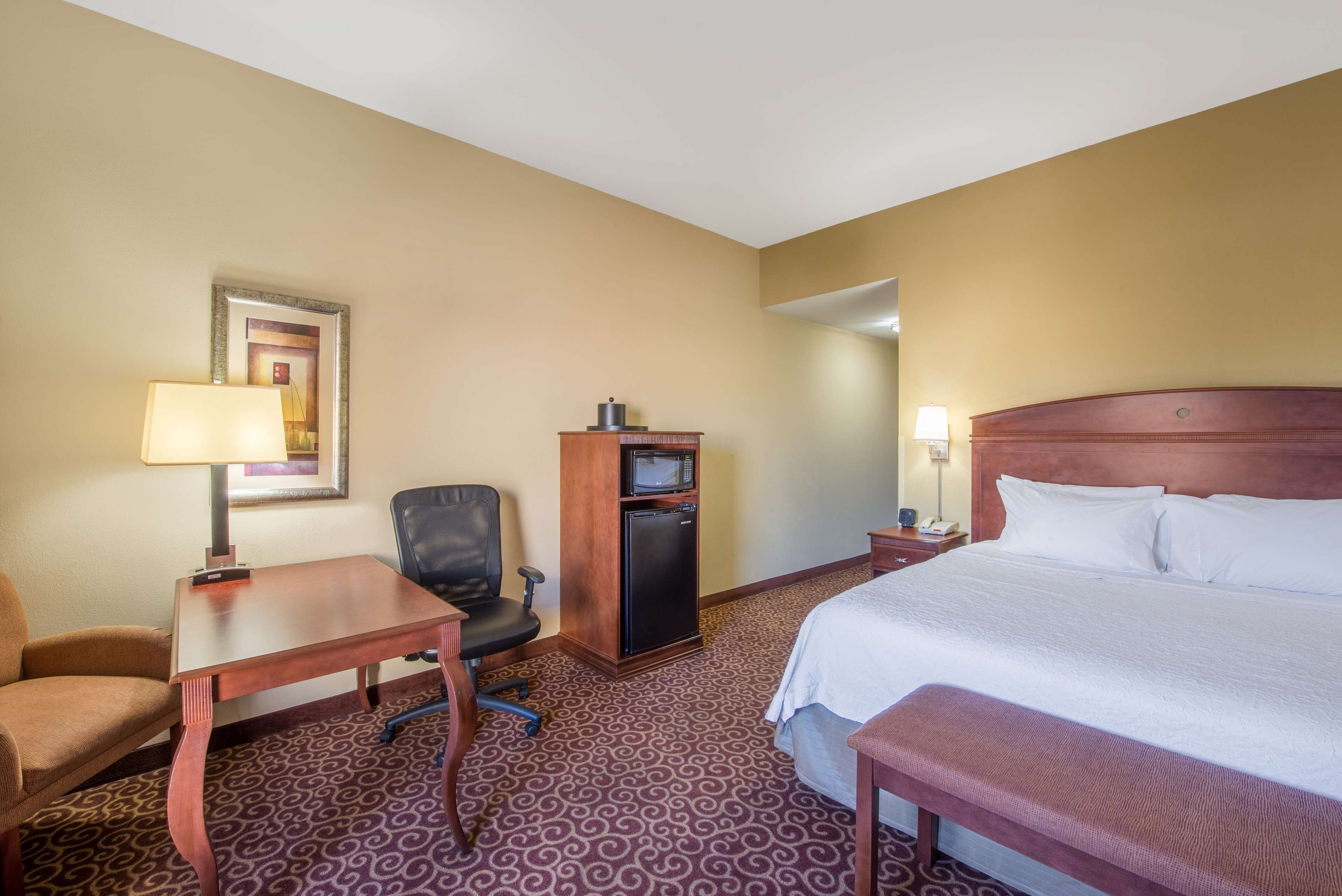 A hotel room with a bed, desk, chair, refrigerator, and a small table.