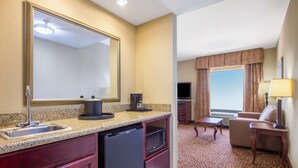 A hotel room with a kitchenette, a large mirror, a flat-screen TV, a sofa, and a patterned carpet. - Hampton Inn & Suites Oklahoma City - South (Oklahoma City)