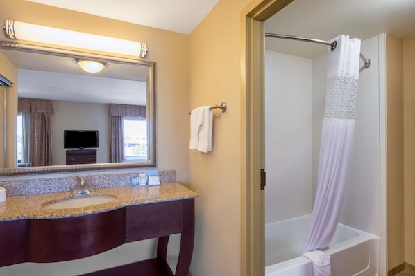 A bathroom with a granite countertop sink, a mirror, a towel rack, and a shower with a white curtain. - Hampton Inn & Suites Oklahoma City - South (Oklahoma City)