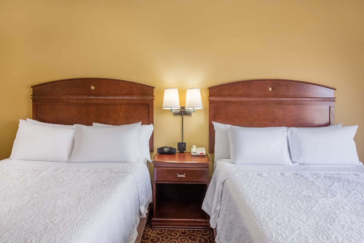 A hotel room with two single beds, a nightstand with a lamp, a phone, and a small table.