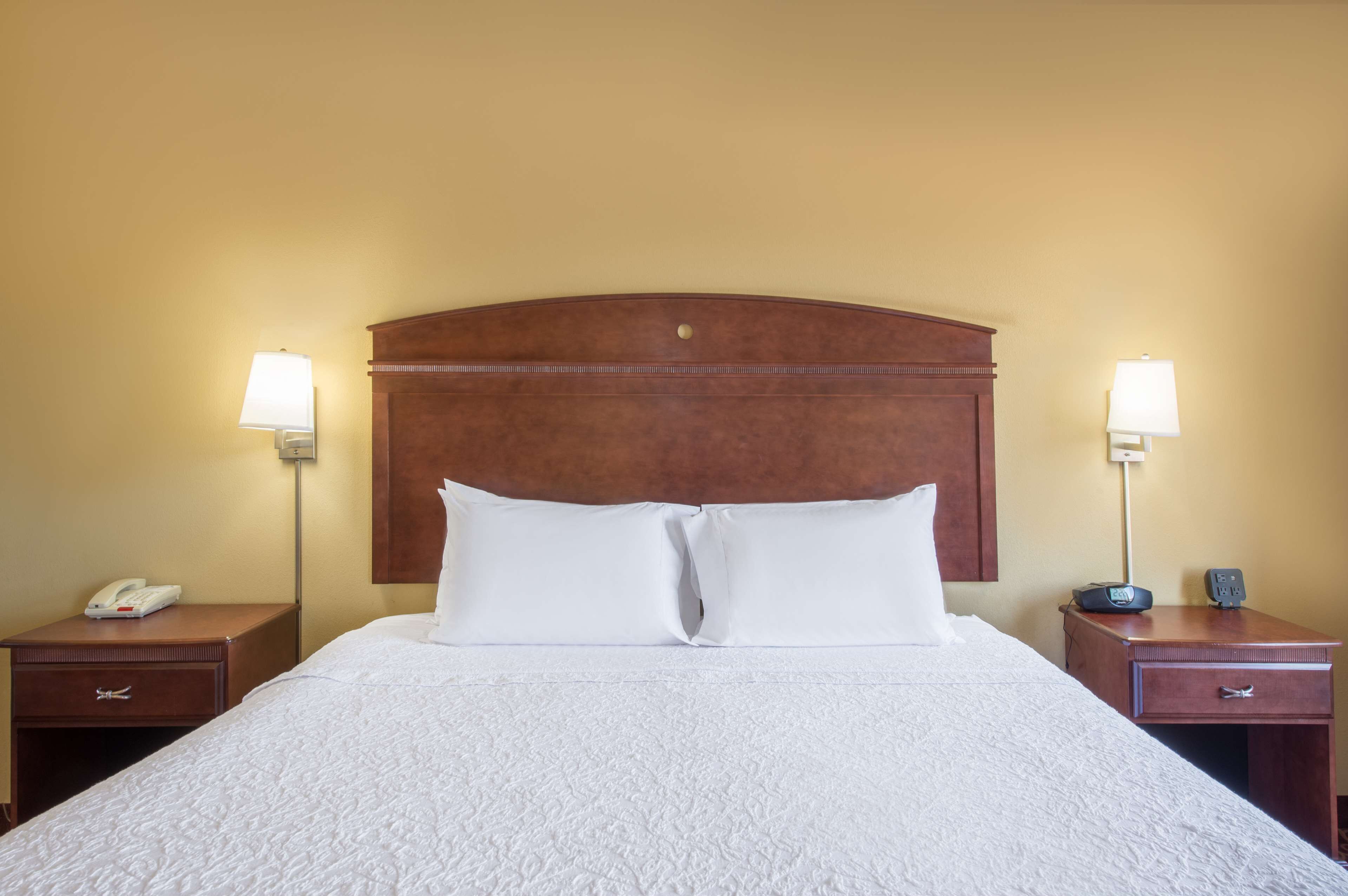 A hotel room with a large bed, two bedside tables, a nightstand, a lamp, and a phone.