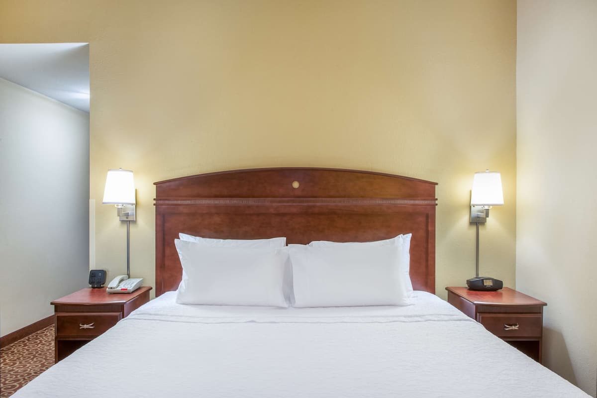 A hotel room with a large bed, two bedside tables, a nightstand, a lamp, and a telephone.