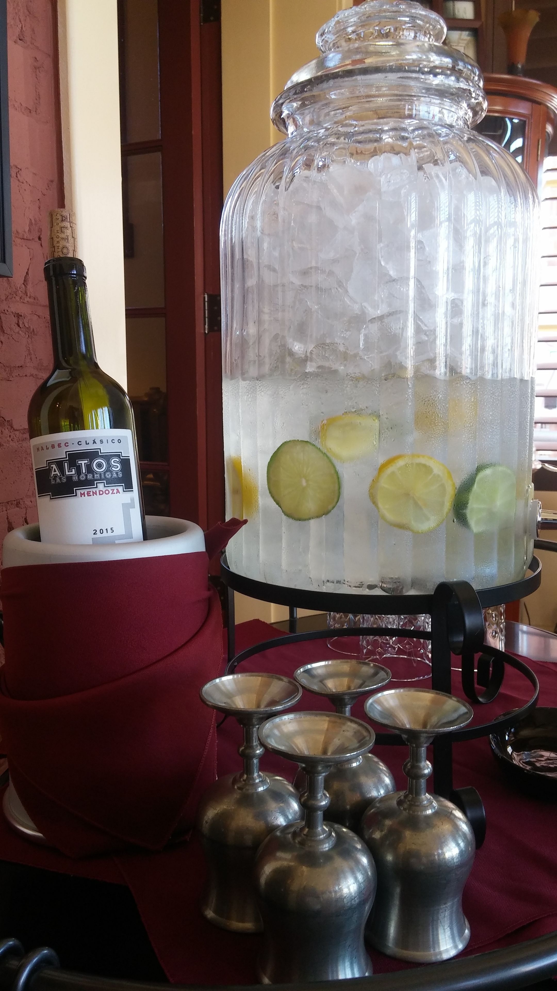 A glass jar with ice and lemon slices, a bottle of wine, and metal salt and pepper shakers on a table.